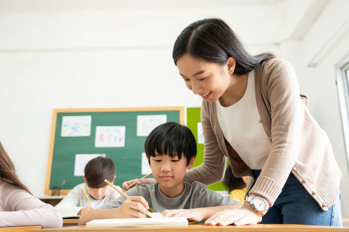 Teacher assisting a young student with his schoolwork in class.