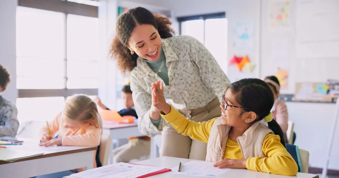 Teacher giving a high-five to a smiling student in classroom.