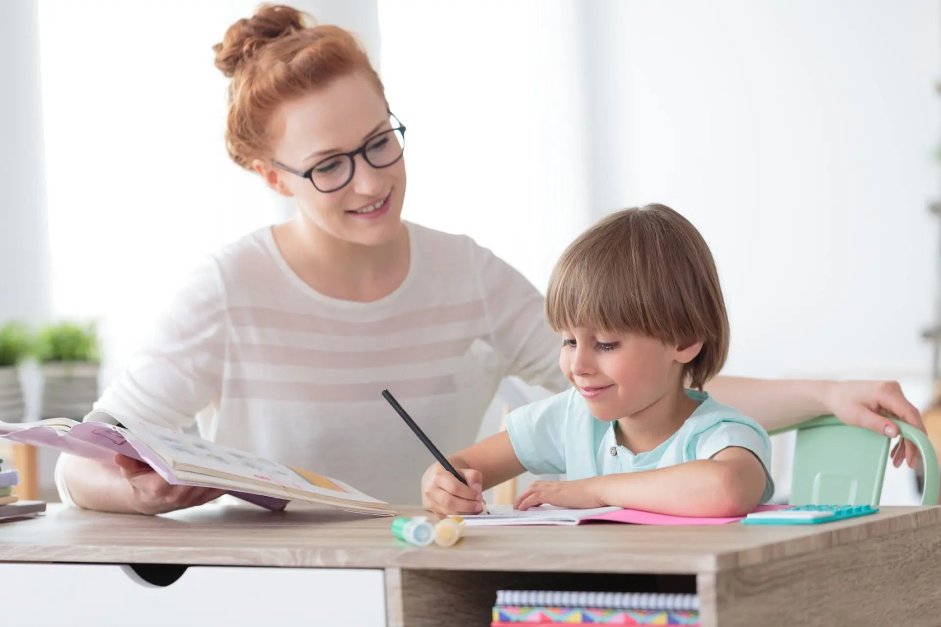 A woman helps a young boy with his homework at a desk.